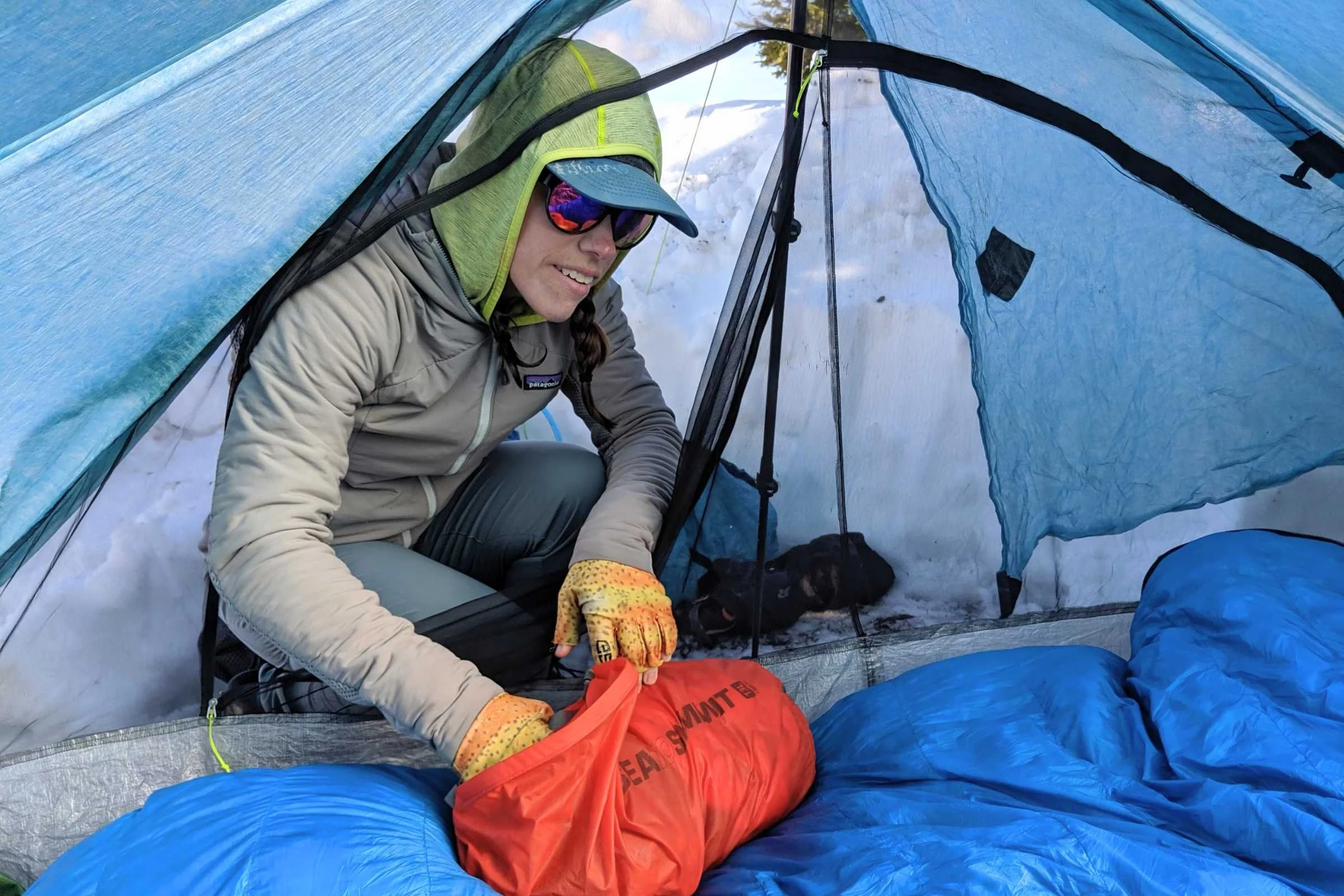 Hands packing a high-loft purple down sleeping bag into a black stuff sack.