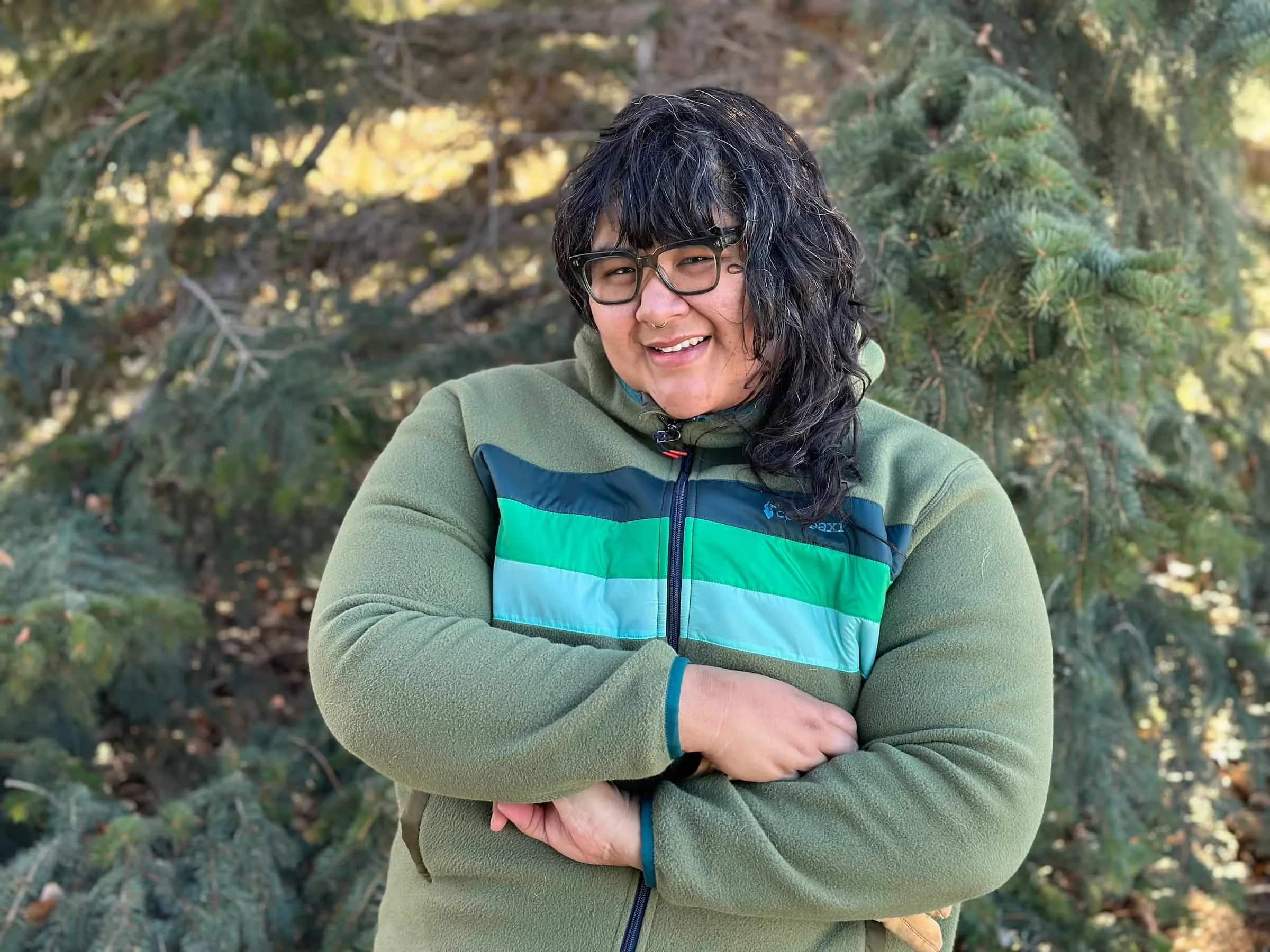 Front view of a hiker wearing a multi-colored Cotopaxi fleece jacket outdoors.