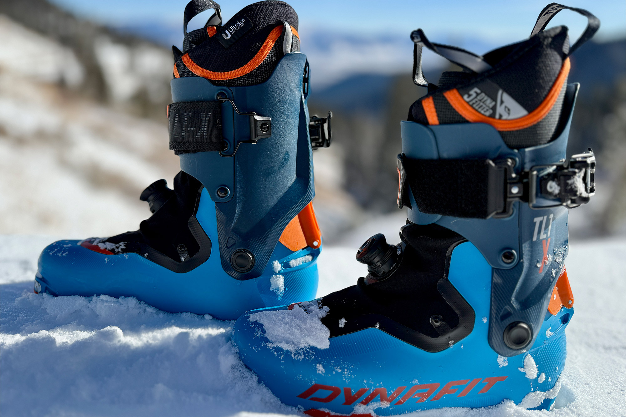 A pair of blue Dynafit TLT X ski boots standing upright in fresh white snow.