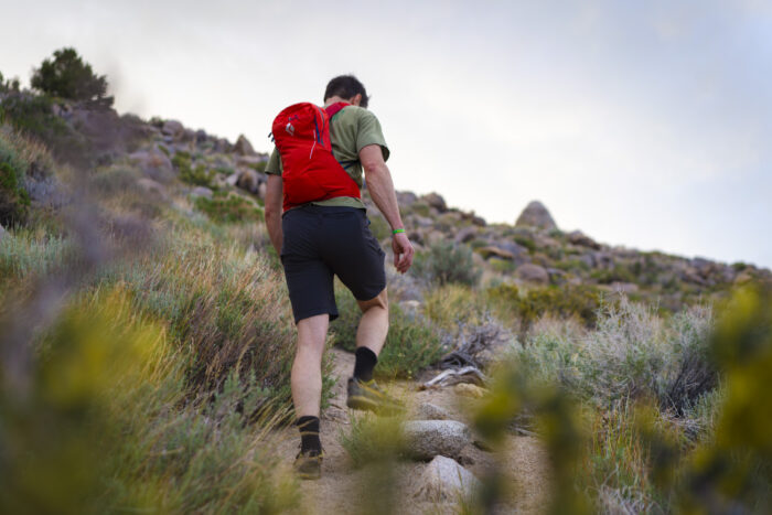 A hiker navigating a steep, rocky trail with a technical daypack.