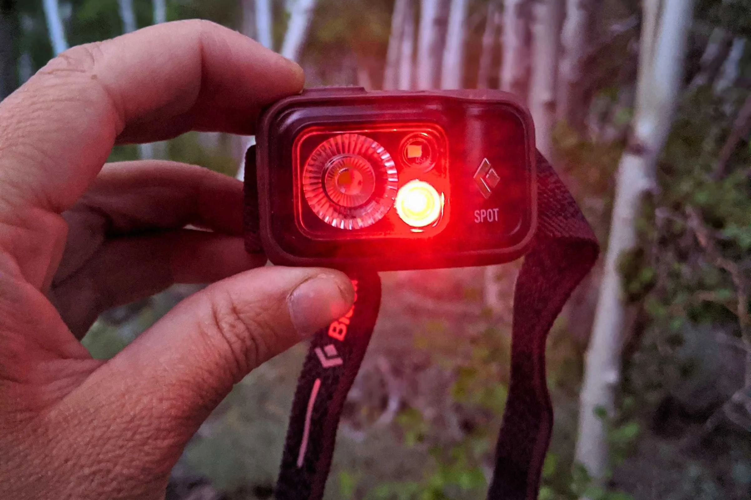 A person in a tent at night using a headlamp set to a soft red light mode.