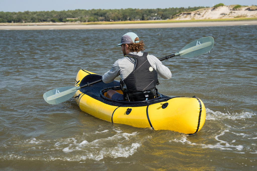 A person paddling the MRS Nomad S1D hybrid packraft on a calm river.
