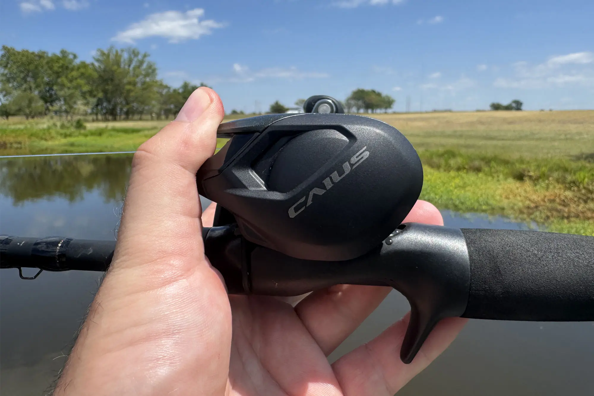 A close-up of a hand comfortably gripping the Shimano Caius casting reel.