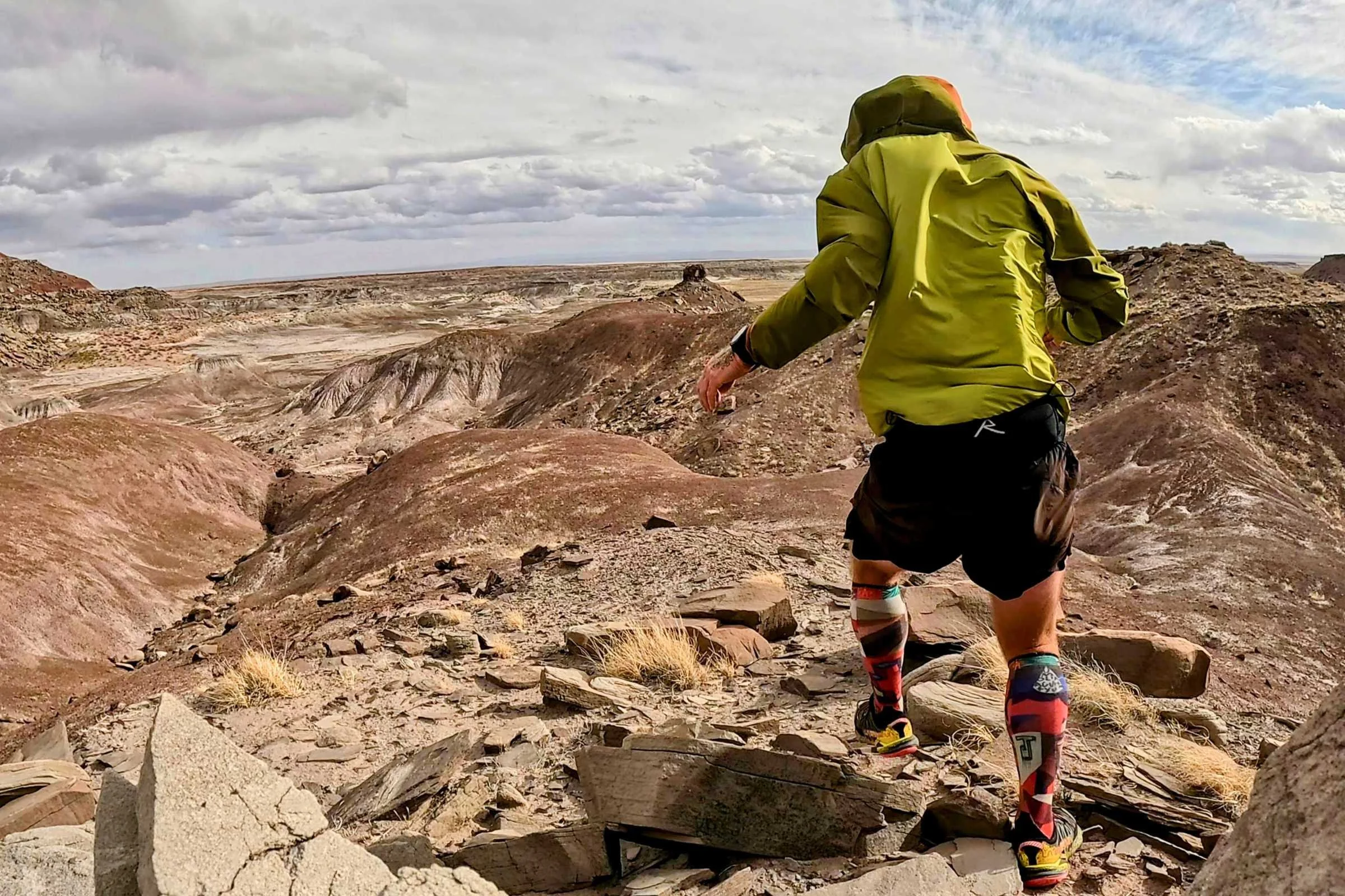 A man hiking on a mountain trail wearing the Mountain Hardwear Kor Airshell Hybrid.