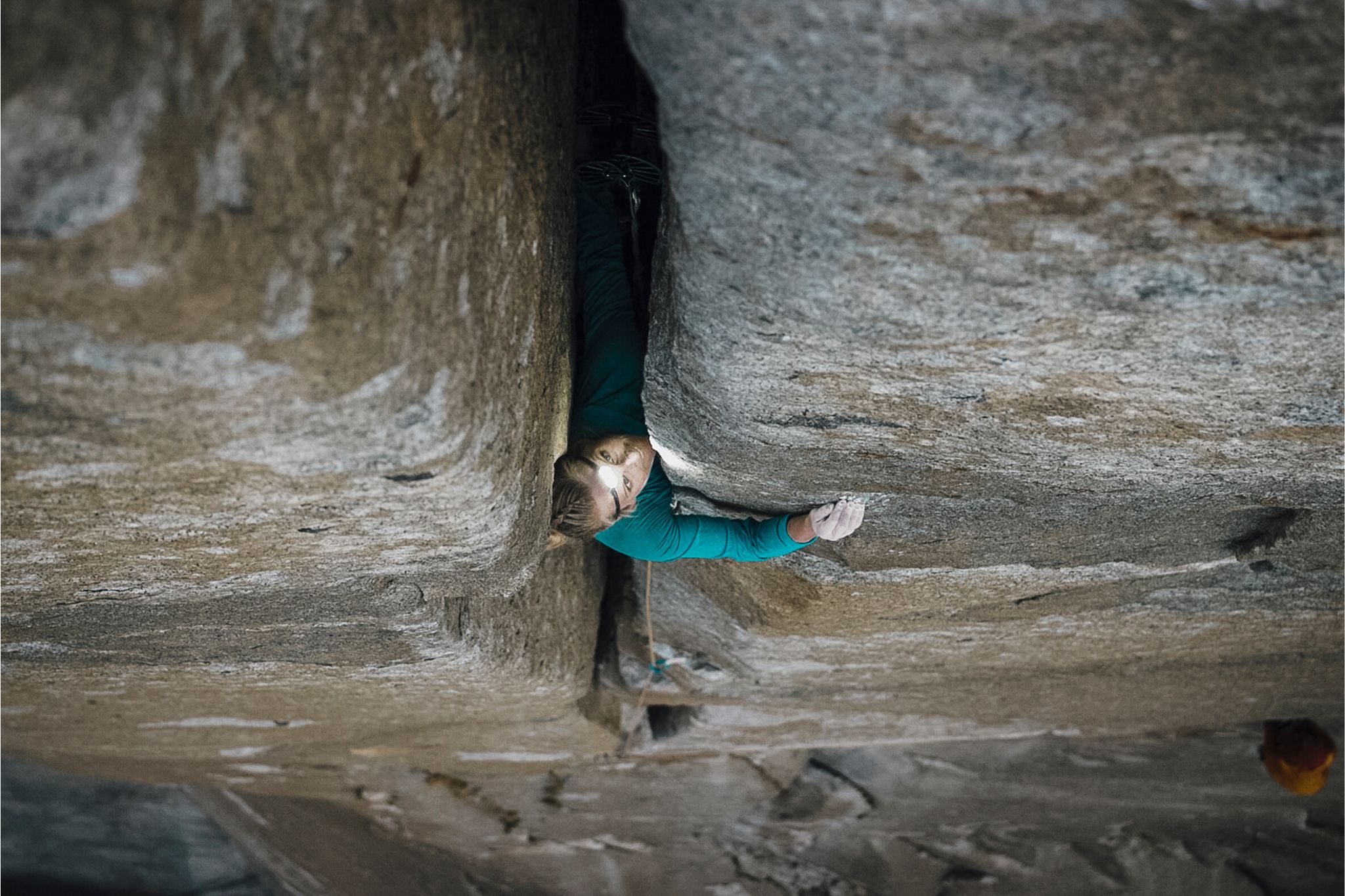A woman in a blue jacket climbs a vertical crack in a granite wall.