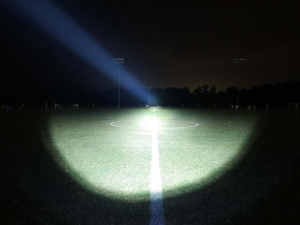 A powerful flashlight beam cutting through the night to illuminate a distant treeline.