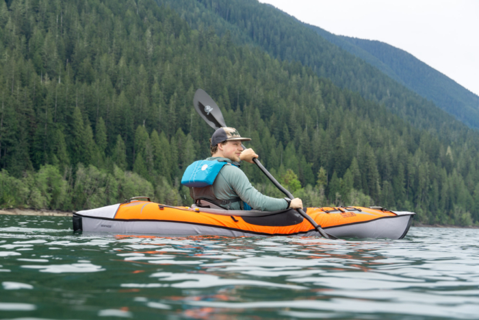 A variety of colorful inflatable kayaks lined up on a grassy shore next to a lake.