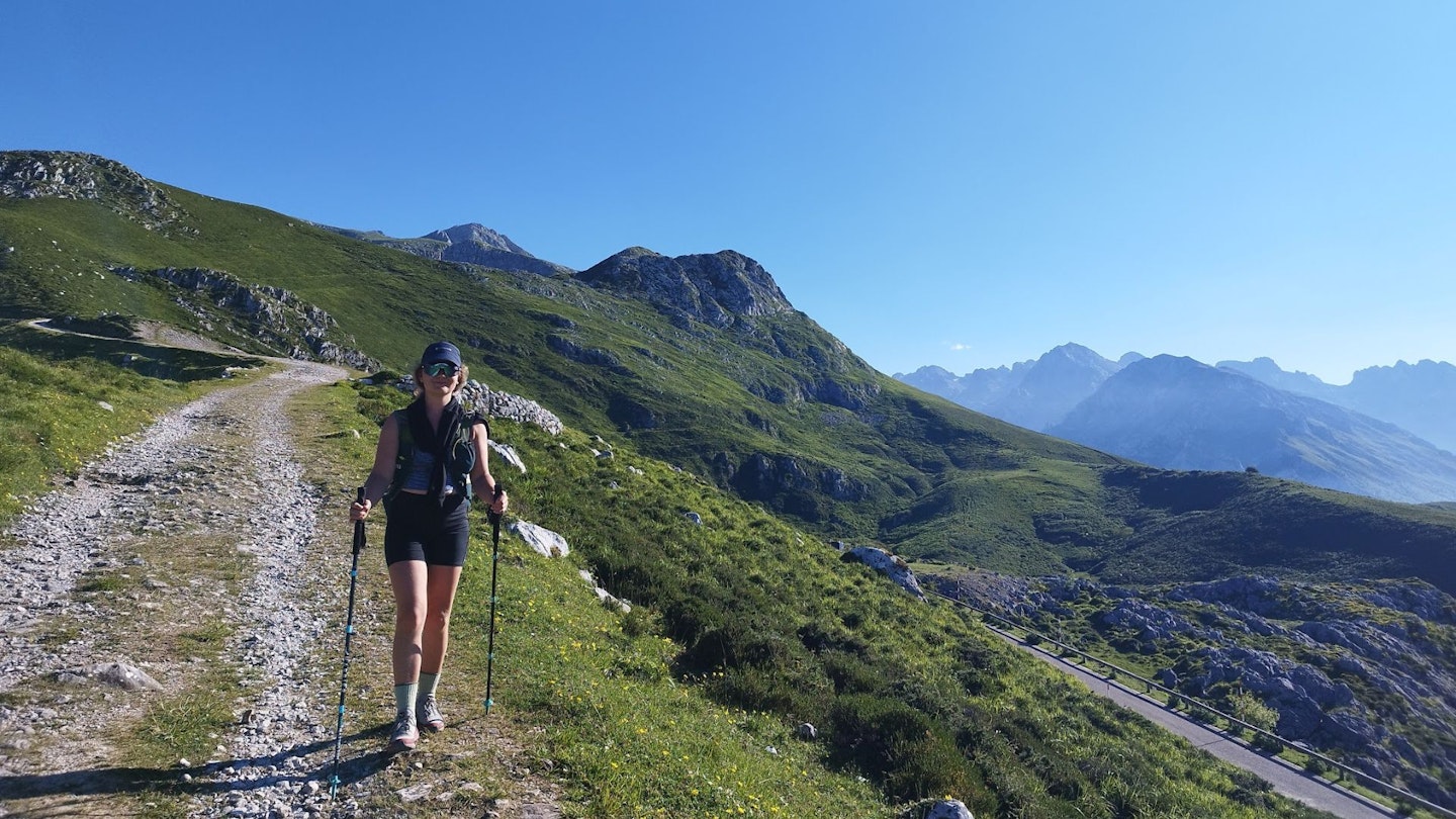 A hiker walking through the green, rocky slopes of the Picos De Europa mountains.