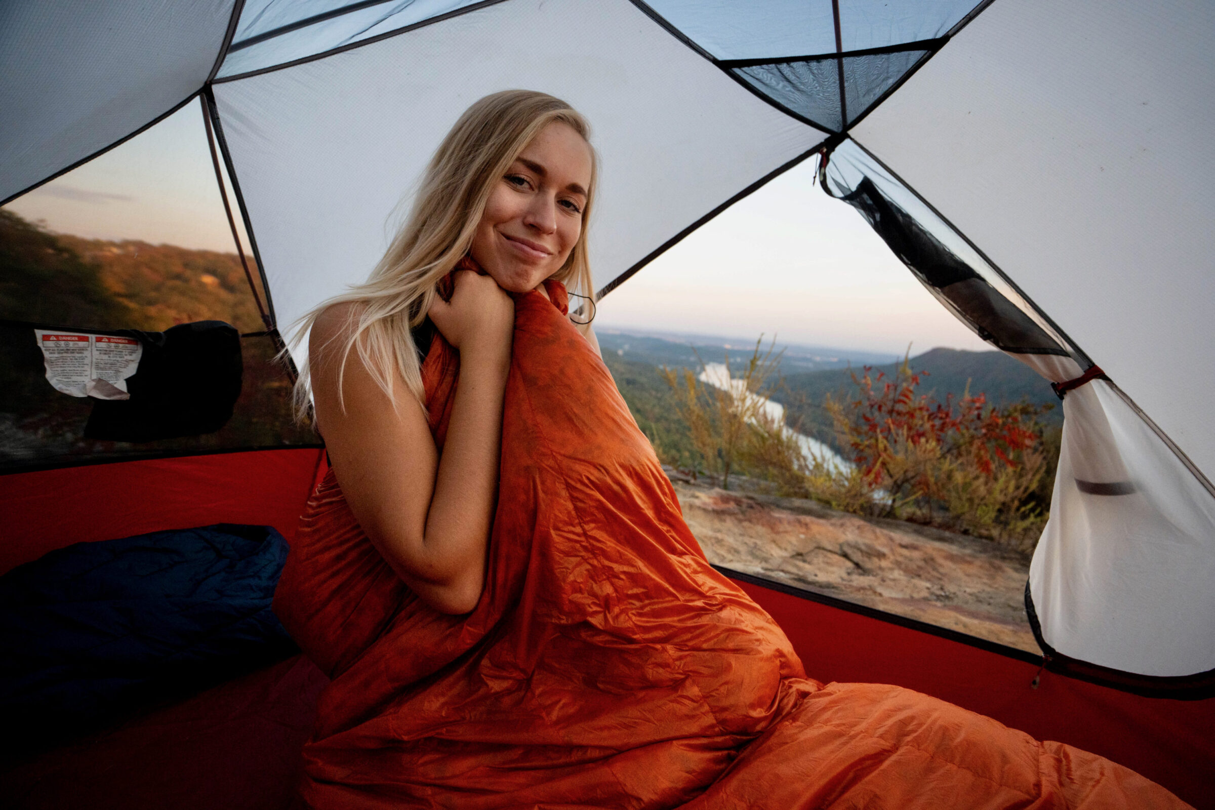 A person testing a sleeping bag on a snowy mountain ridge.