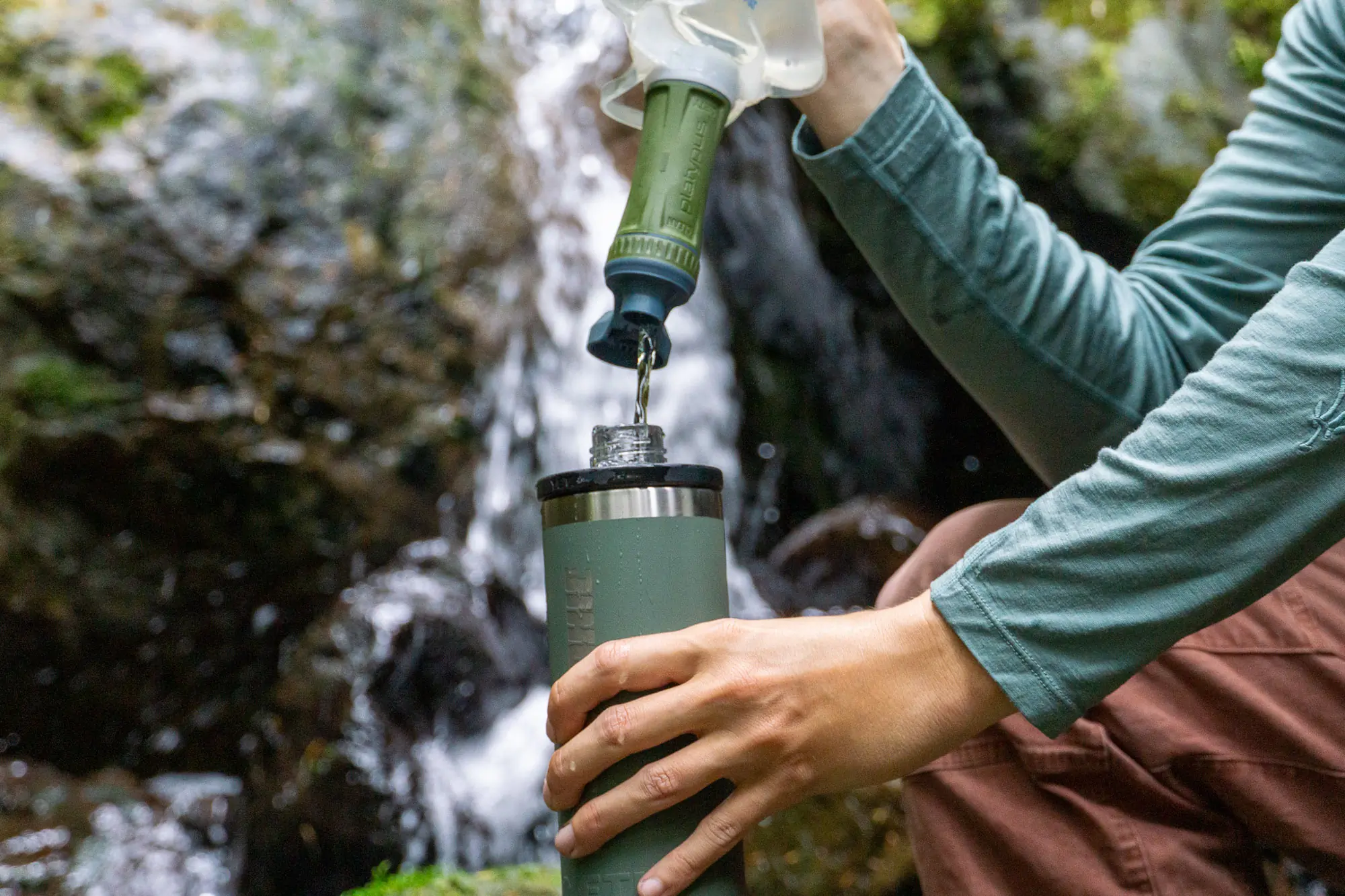A hiker using a squeeze-style water filter to collect water from a natural mountain stream