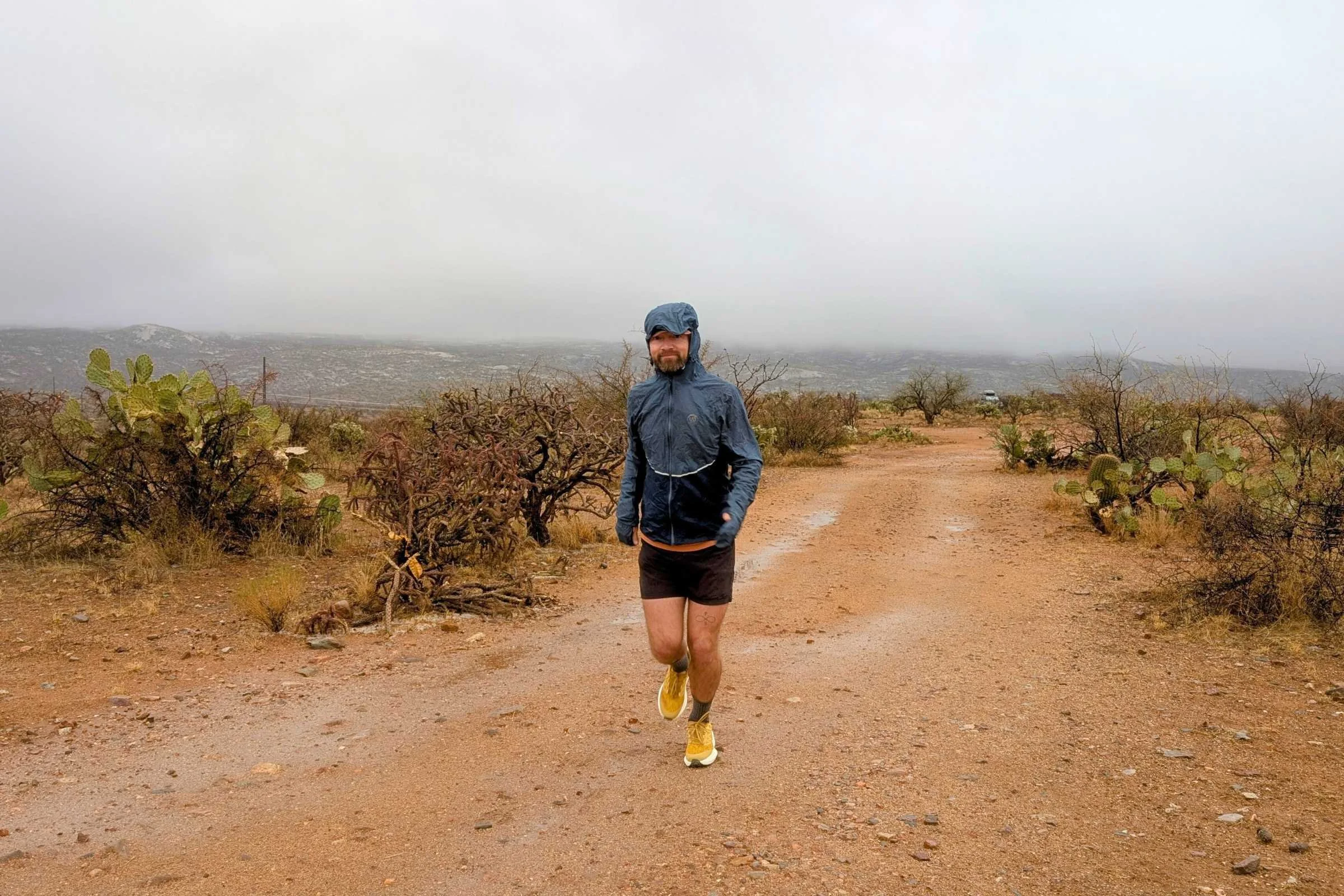 A runner wearing the Ultimate Direction Ultra II waterproof jacket on a mountain trail.