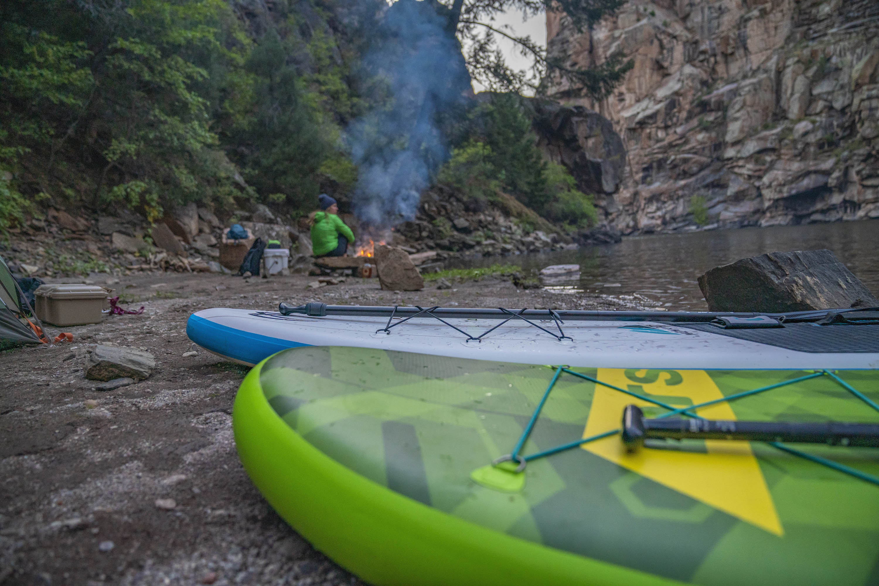 A rigid paddleboard on a shoreline packed with waterproof camping bags and gear.