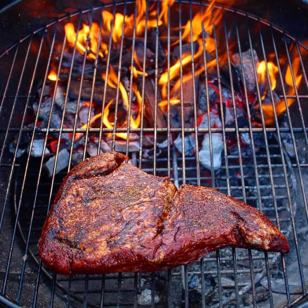 A seasoned cast iron skillet cooking over a vibrant campfire flame.