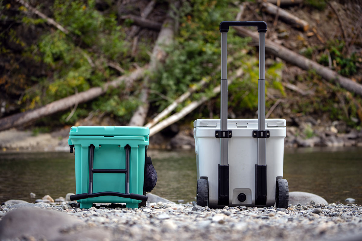 Two coolers side-by-side comparing a rigid metal haul handle and a telescoping plastic handle.