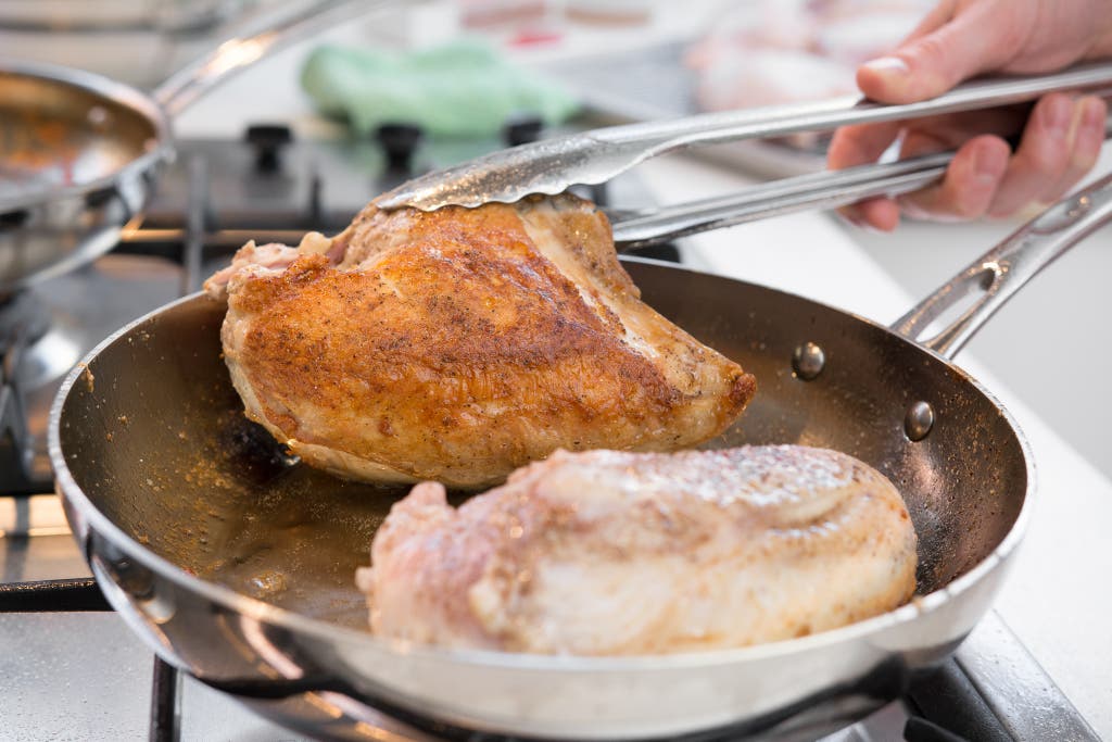 A close-up of chicken browning evenly in a high-quality stainless steel skillet.