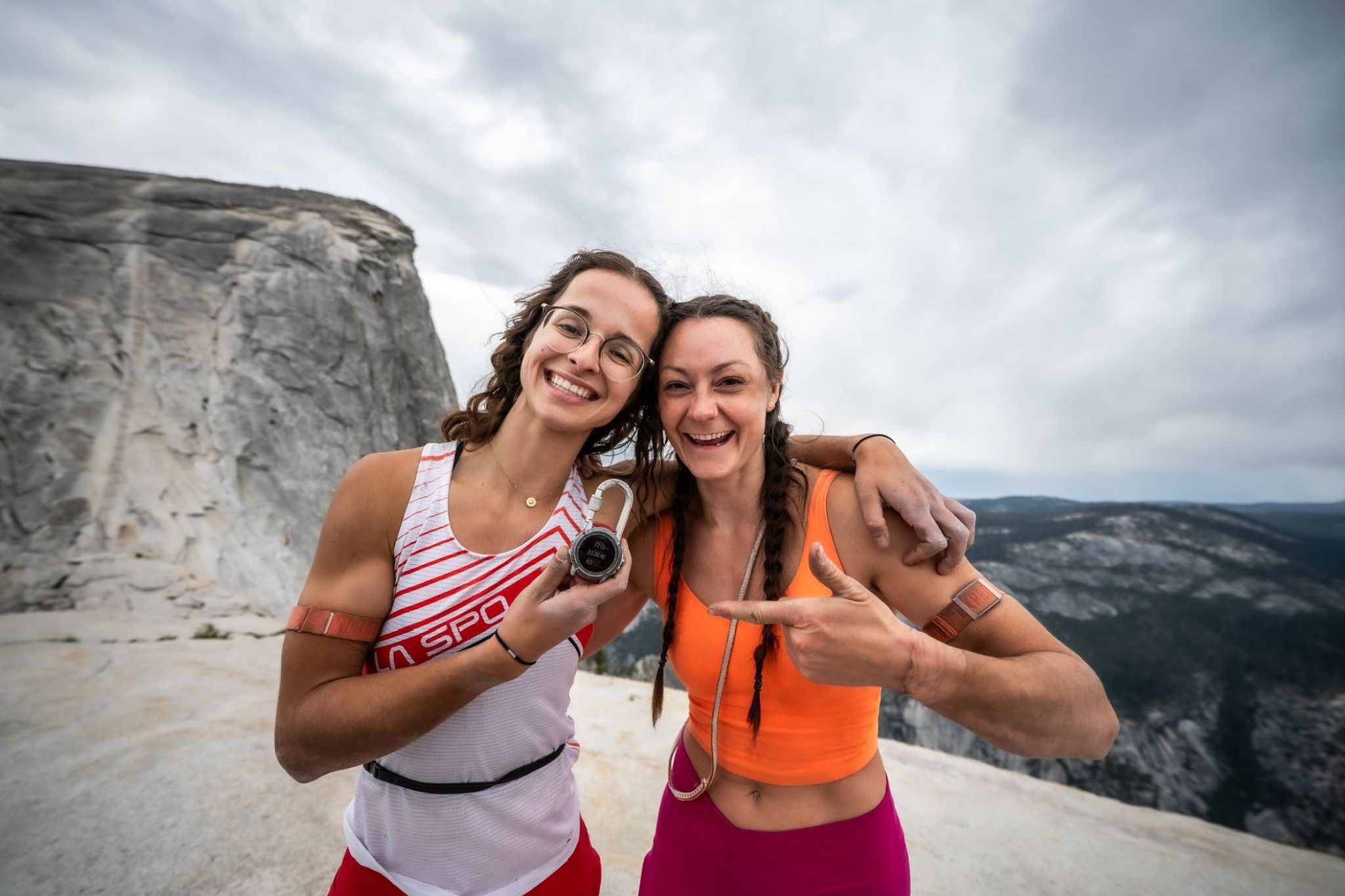 Two women celebrating together on a rocky mountain summit.