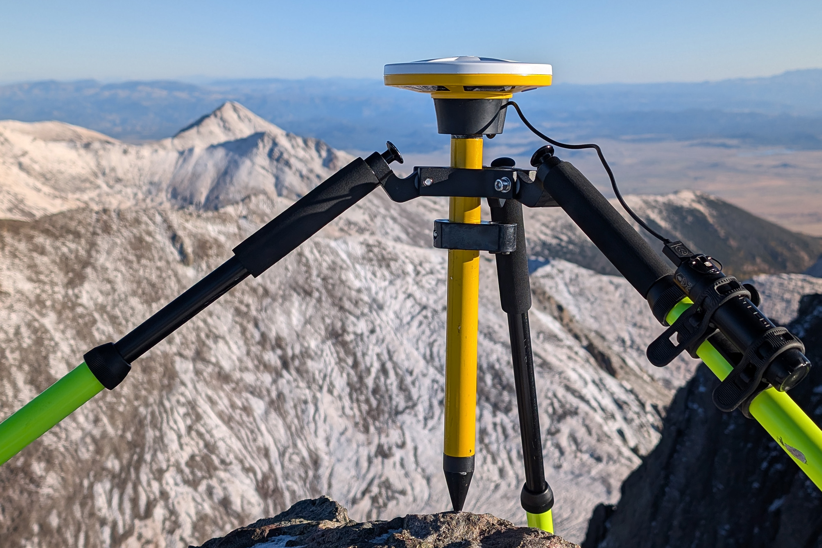 An expedition team member monitors data logging equipment while sitting on a high-altitude mountain summit.