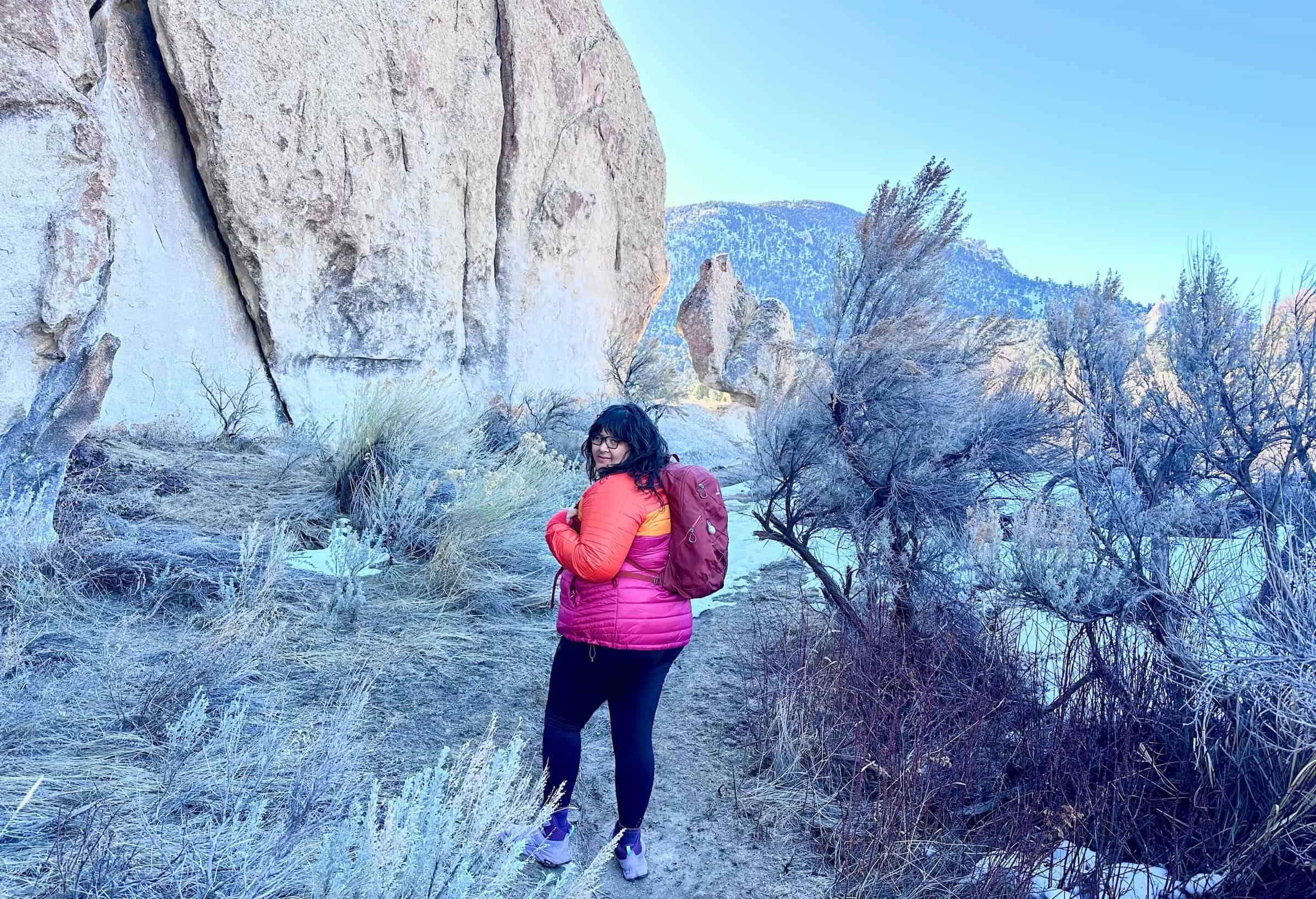 A hiker wearing a blue insulated Cotopaxi Capa jacket in an outdoor setting.
