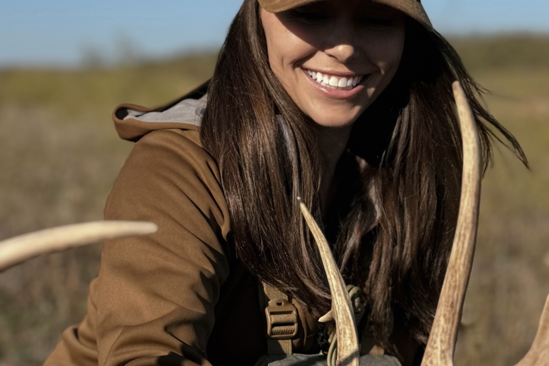 A women's hunting jacket displayed against a natural forest background.