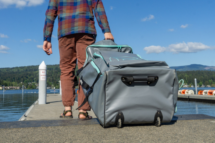 An inflatable kayak completely deflated and folded into a compact wheeled backpack.