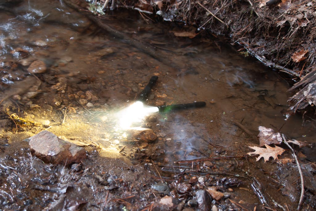Two flashlights fully submerged and turned on in a shallow moving stream.