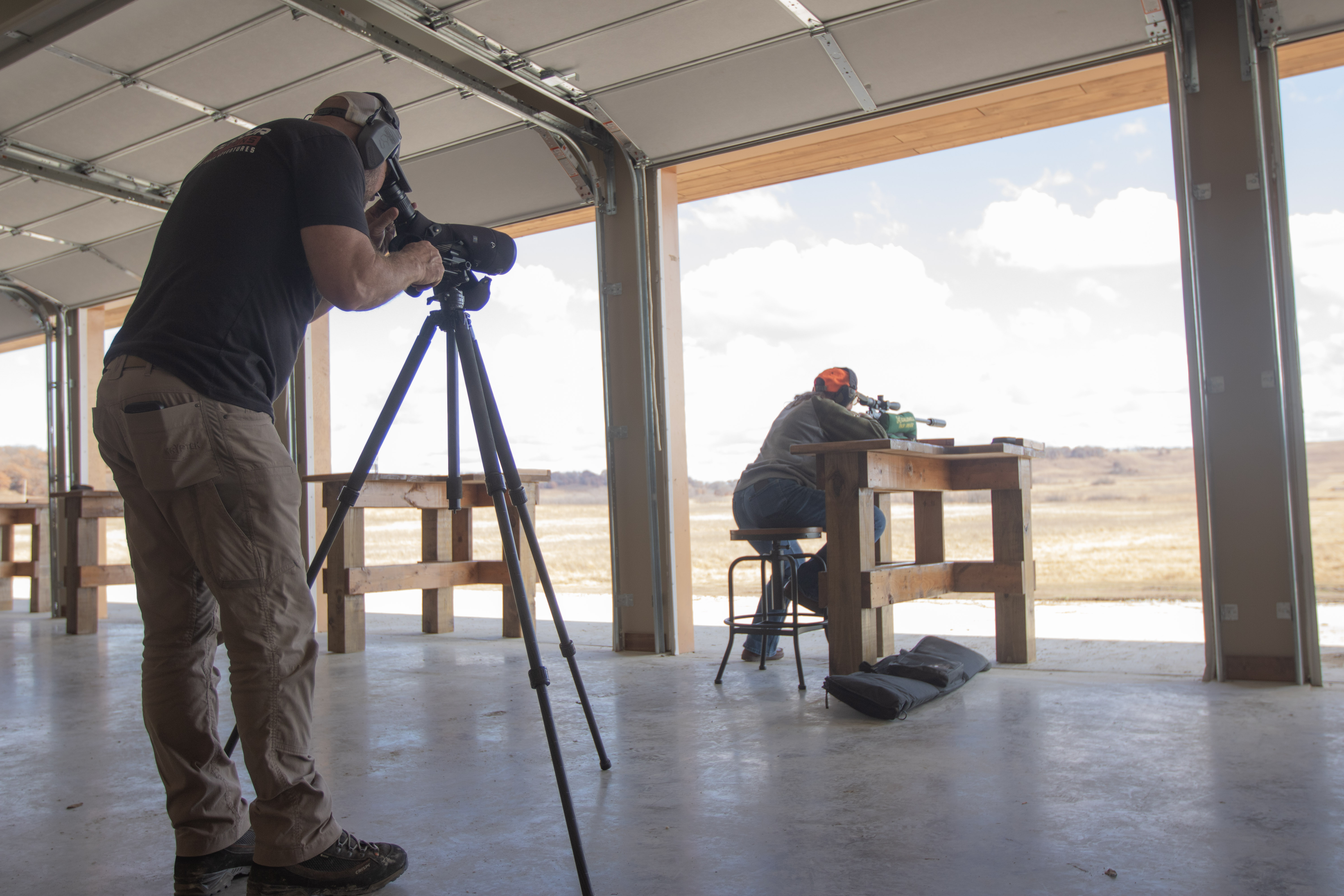 A female student practicing long-range shooting with a professional spotter at a rifle range.