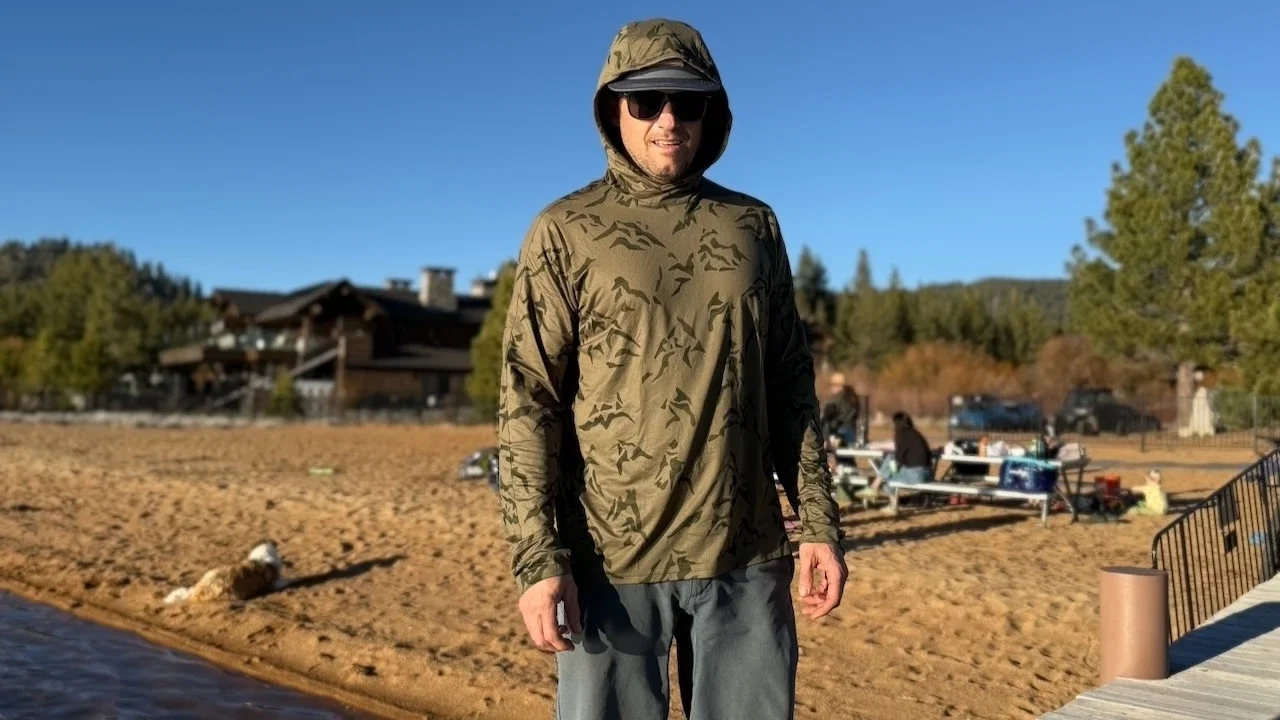 A hiker wearing the REI Sahara Shade hoodie while relaxing at a lake.