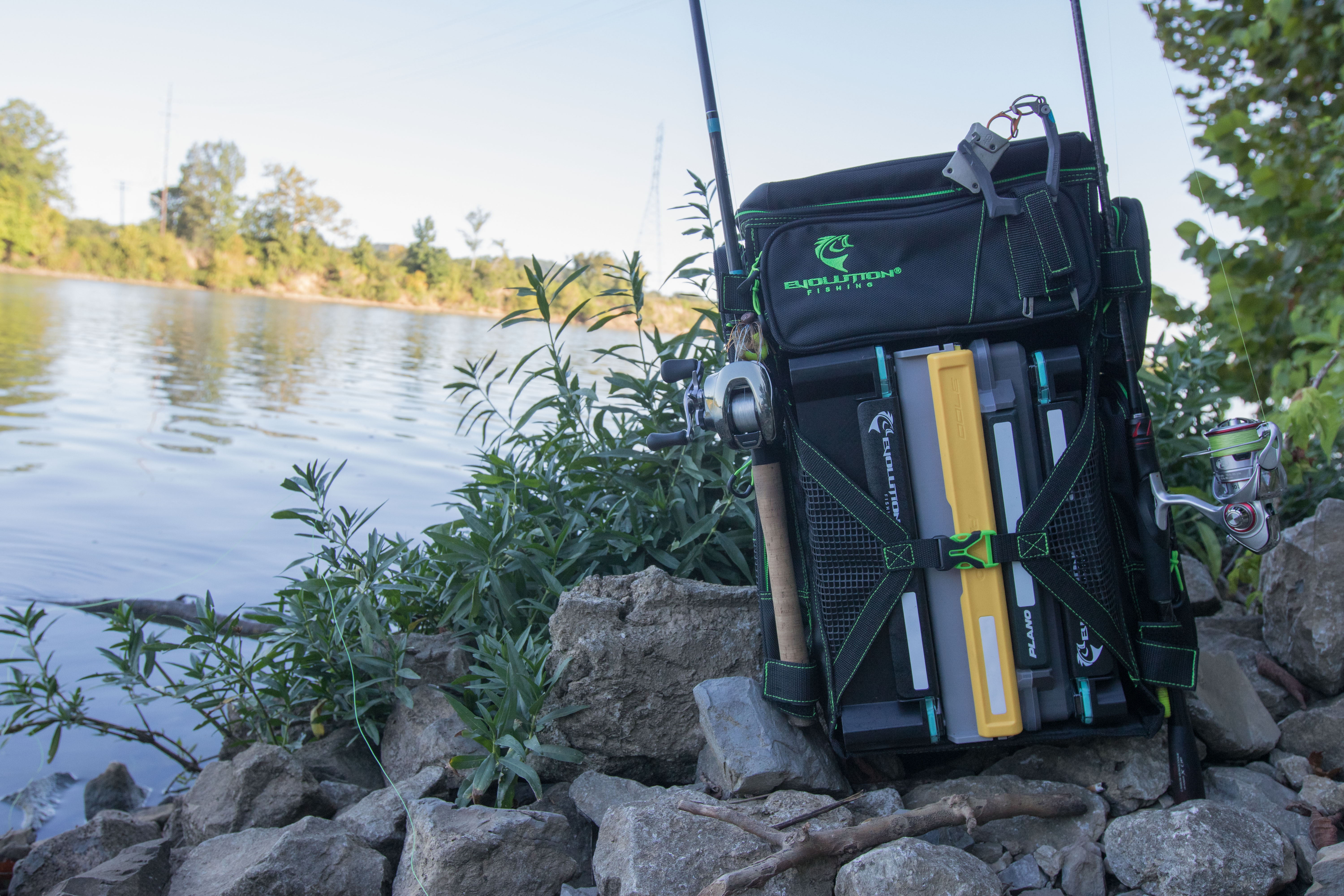 The Evolution Fishing Drift Series tackle backpack sitting outdoors by a riverbank.
