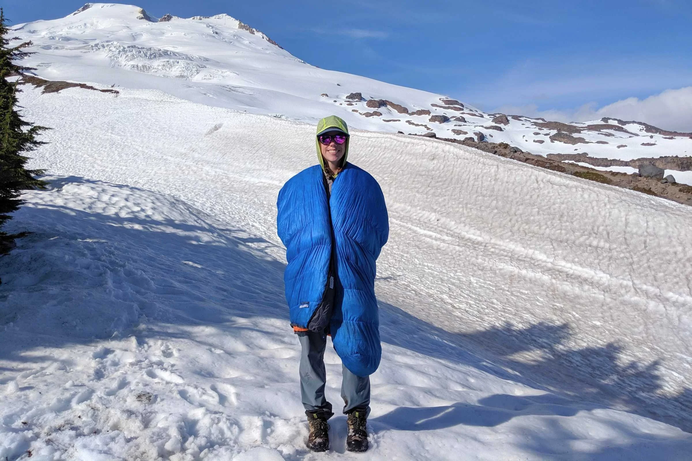 A backpacker wrapped in a red and black sleeping bag over their shoulders for warmth at camp.
