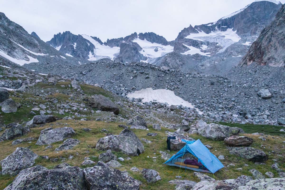 A white Zpacks Duplex Lite tent pitched in a rocky, high-alpine basin with mountains in the background.