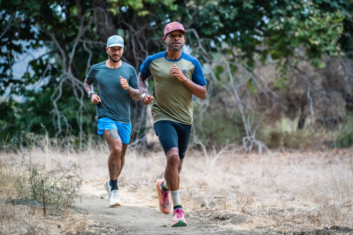 The lower legs of two runners wearing crew-length athletic socks on a dirt trail.