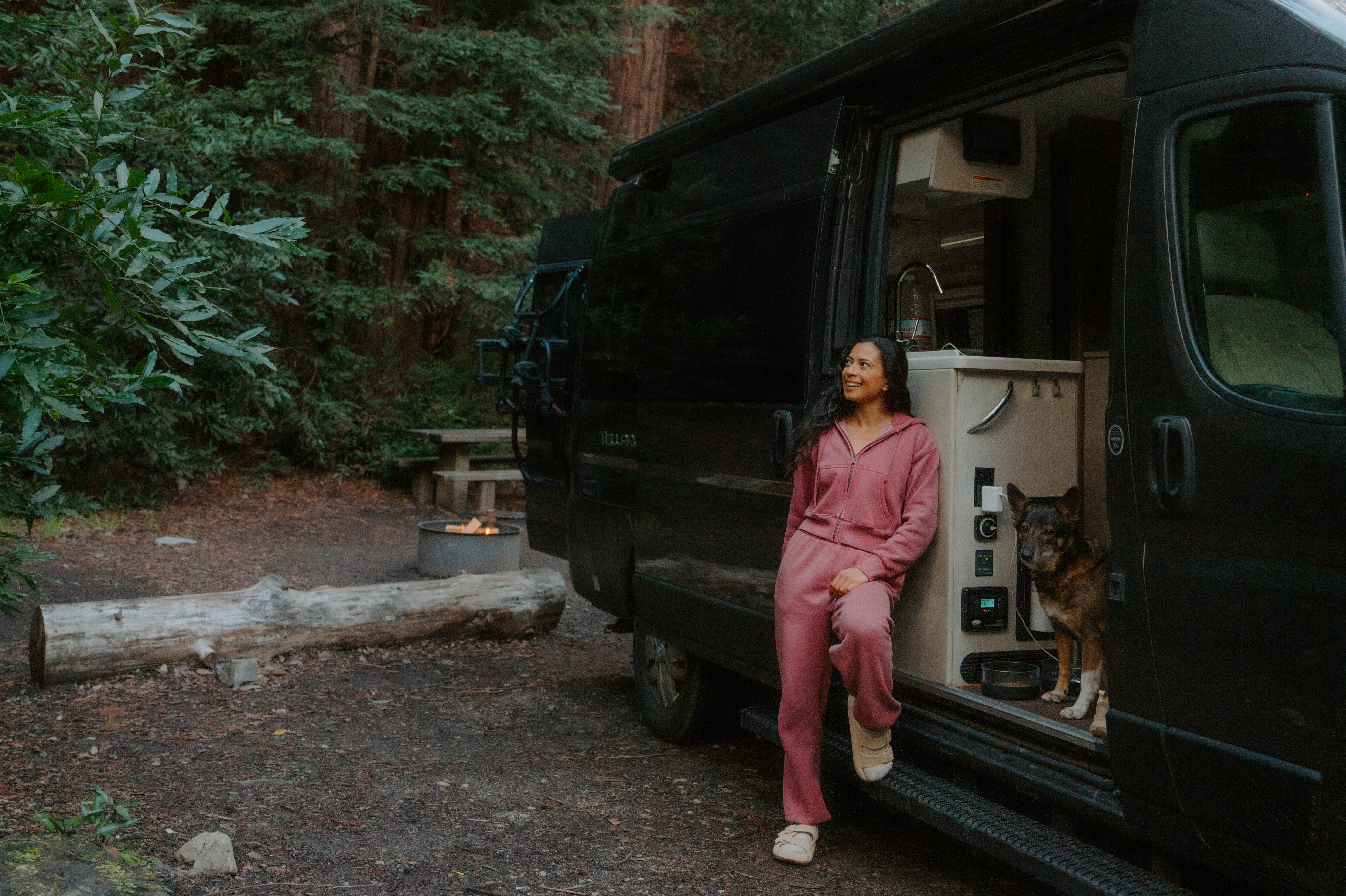 A woman and her dog standing by the side door of a compact adventure van.