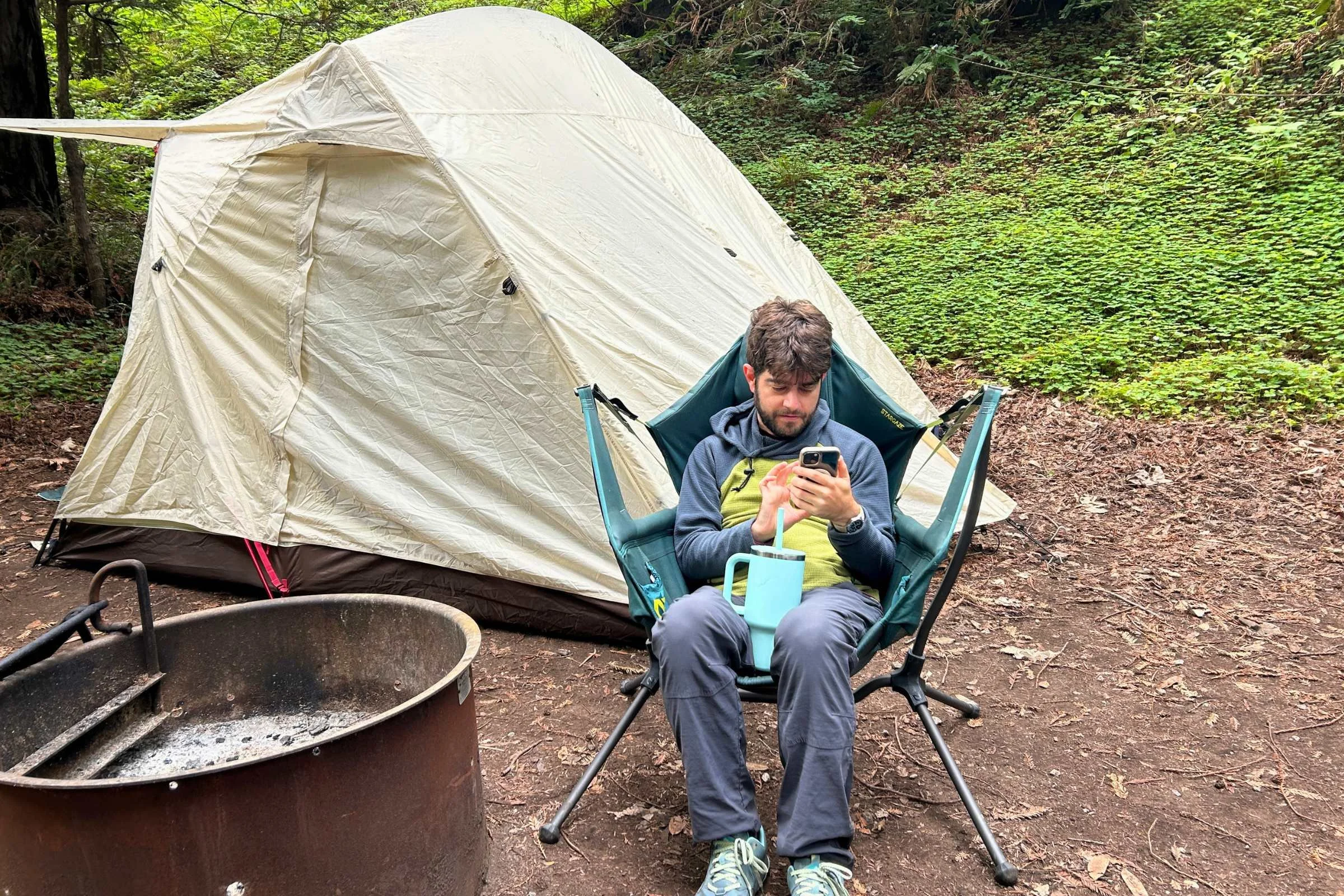 A camper sitting in a chair outside a large camping tent, enjoying the campsite atmosphere.
