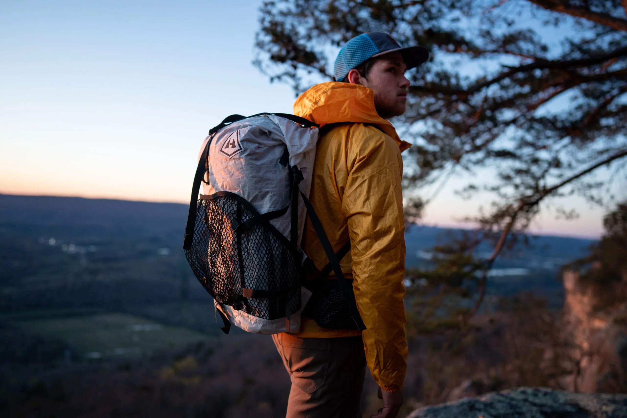 A man wearing a yellow windbreaker and a large backpack hiking through a forest trail.