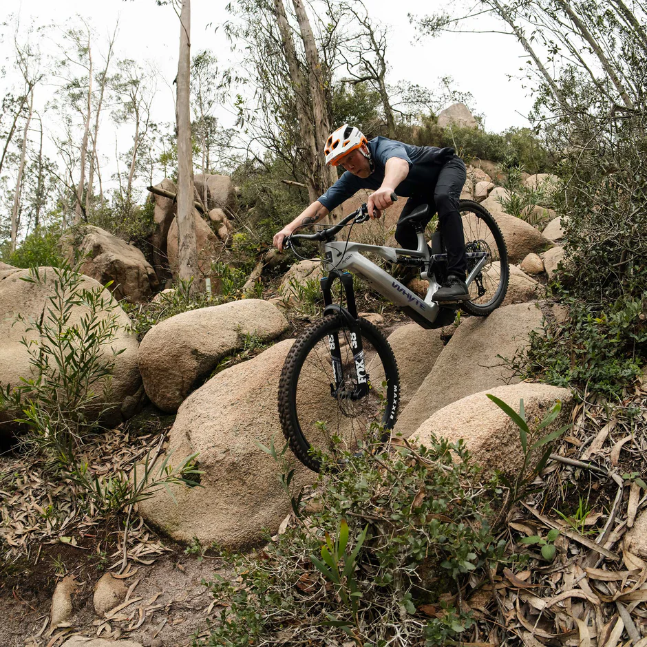 A full-suspension mountain bike navigating through a technical, rocky section of trail.
