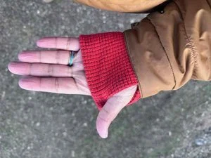 Close-up of a hiker's hand using the thumb hole on a blue technical fleece sleeve.