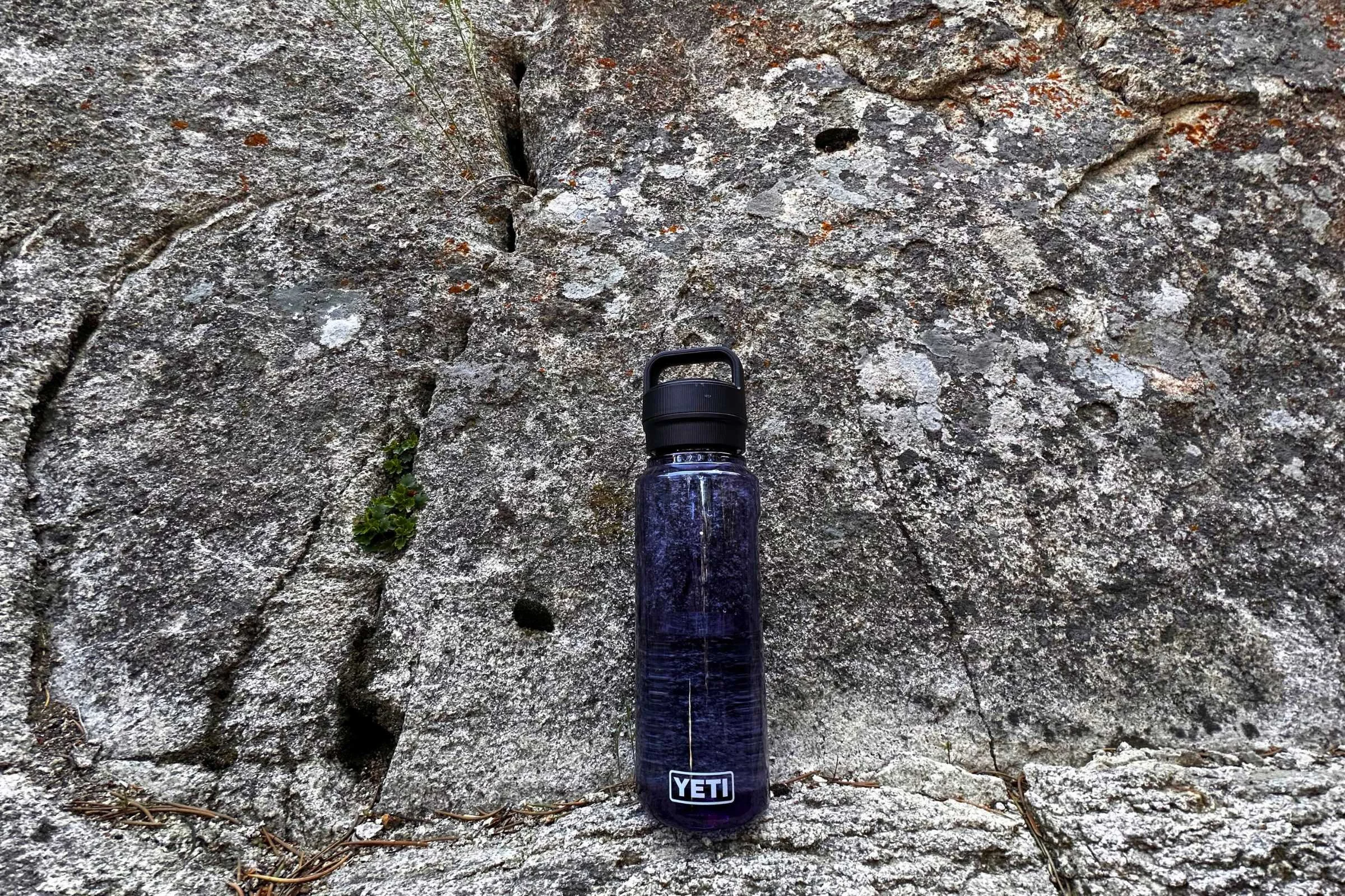 A YETI water bottle placed on sharp, jagged rocks to demonstrate durability.