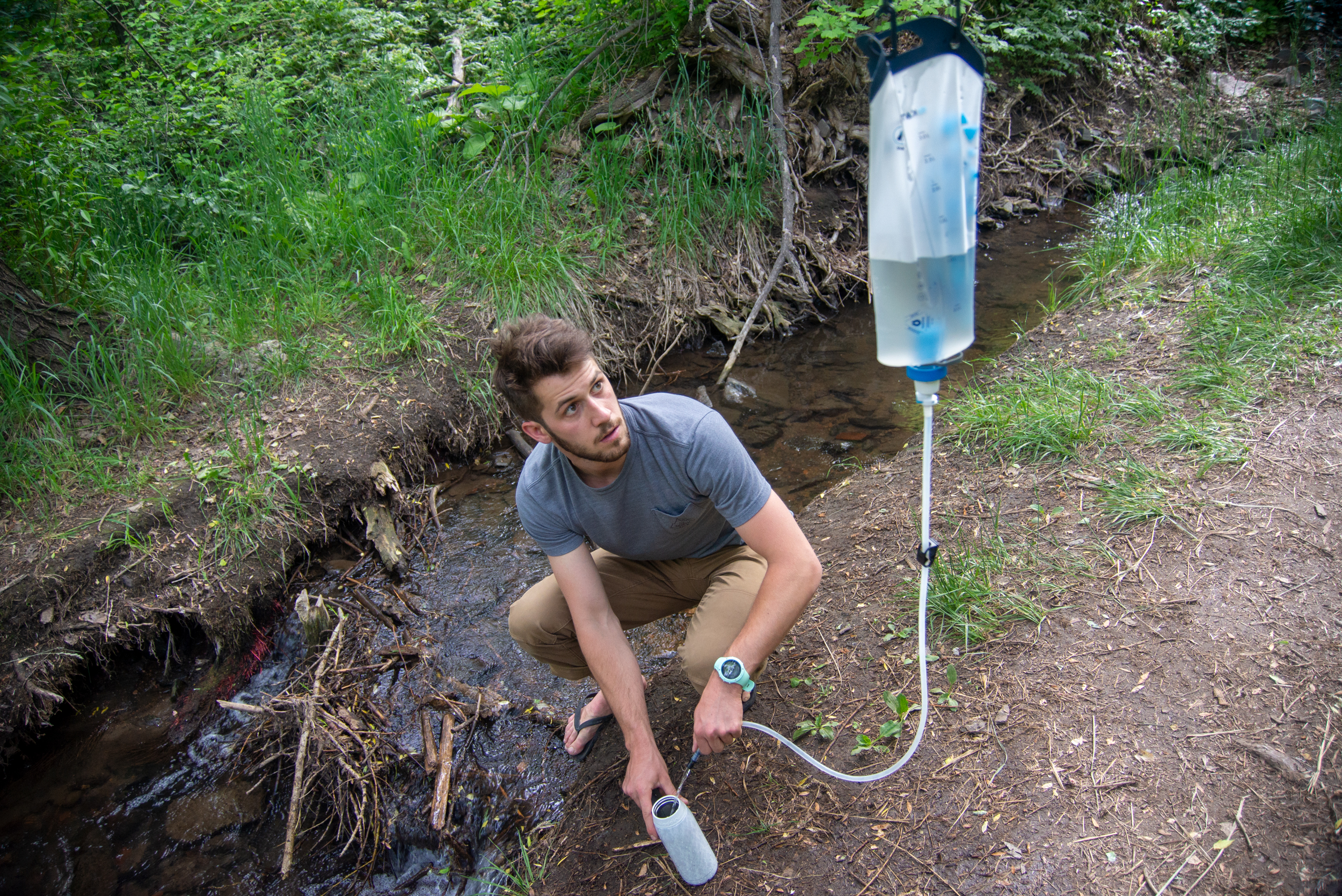 A large gravity water filter bag hanging from a tree branch in a forest