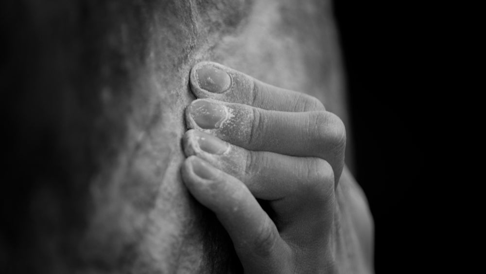 Close-up of a climber's chalk-covered hands gripping a thin rock ledge