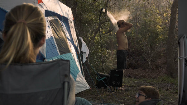 A camper using a pressurized portable shower system next to their vehicle in the outdoors.