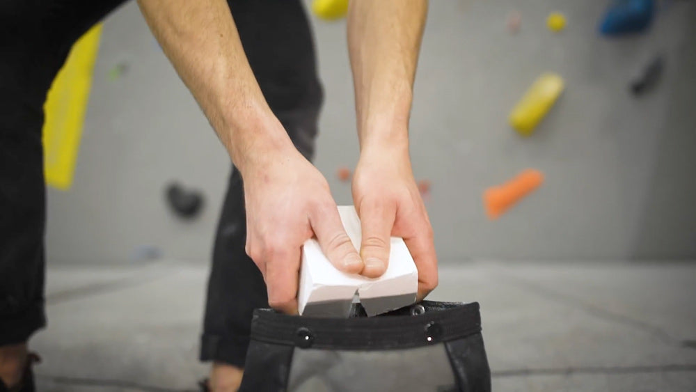 A climber breaking a white block of chalk into a large bouldering bucket
