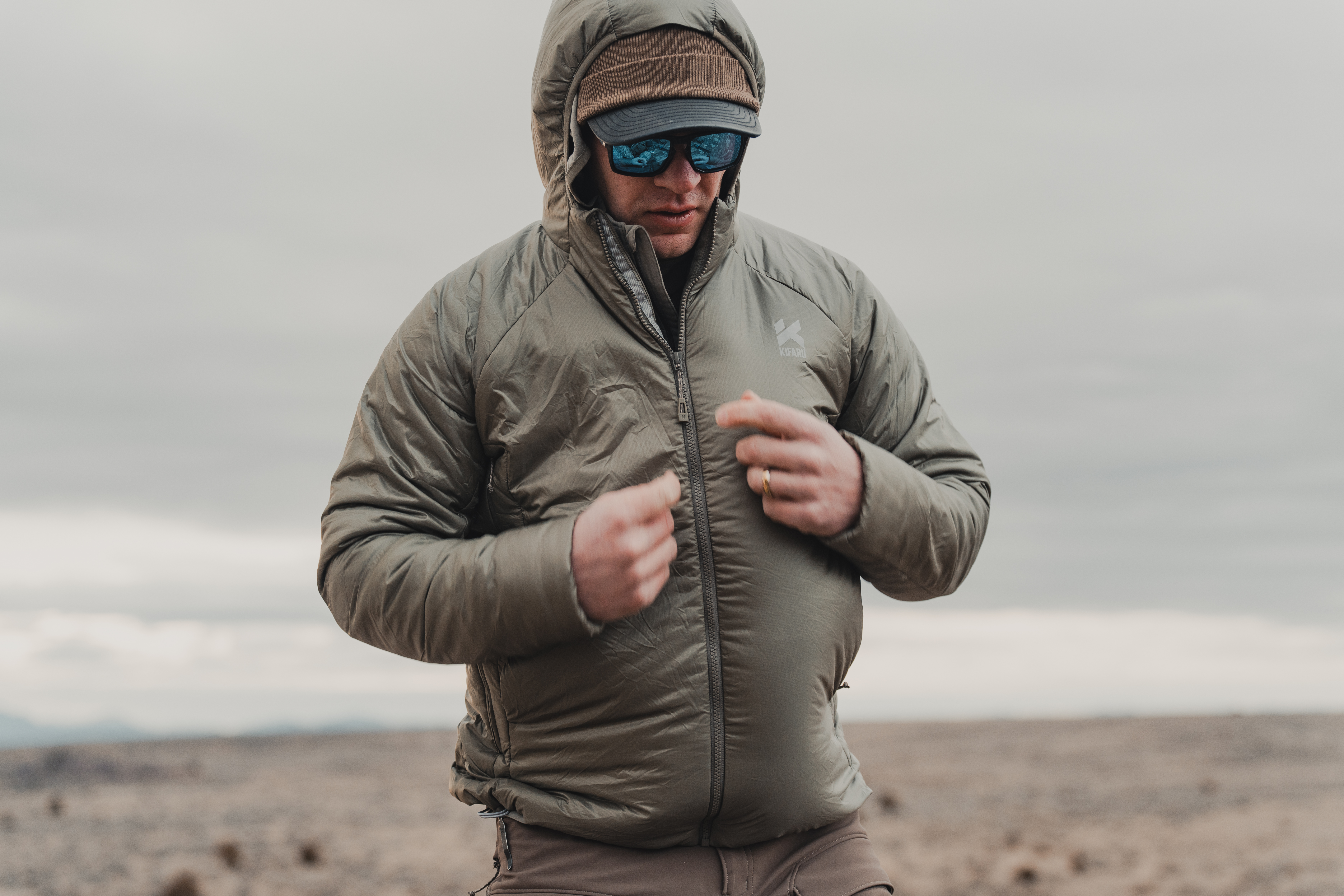 Hunter zipping up his Kifaru jacket while standing in a cold, windy field.