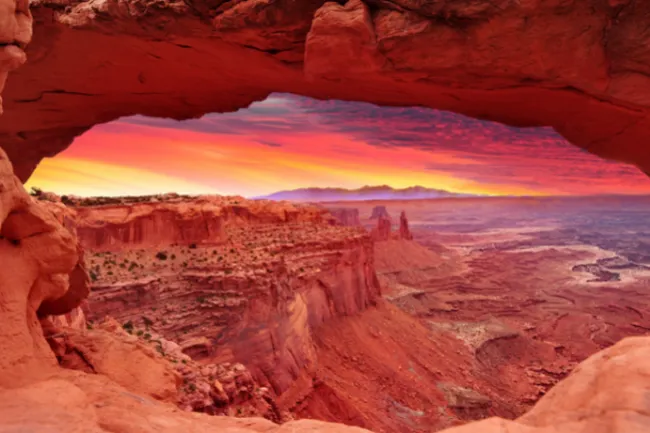 The sun rising over the distant horizons of the Utah desert, casting a warm glow on the canyon rims.