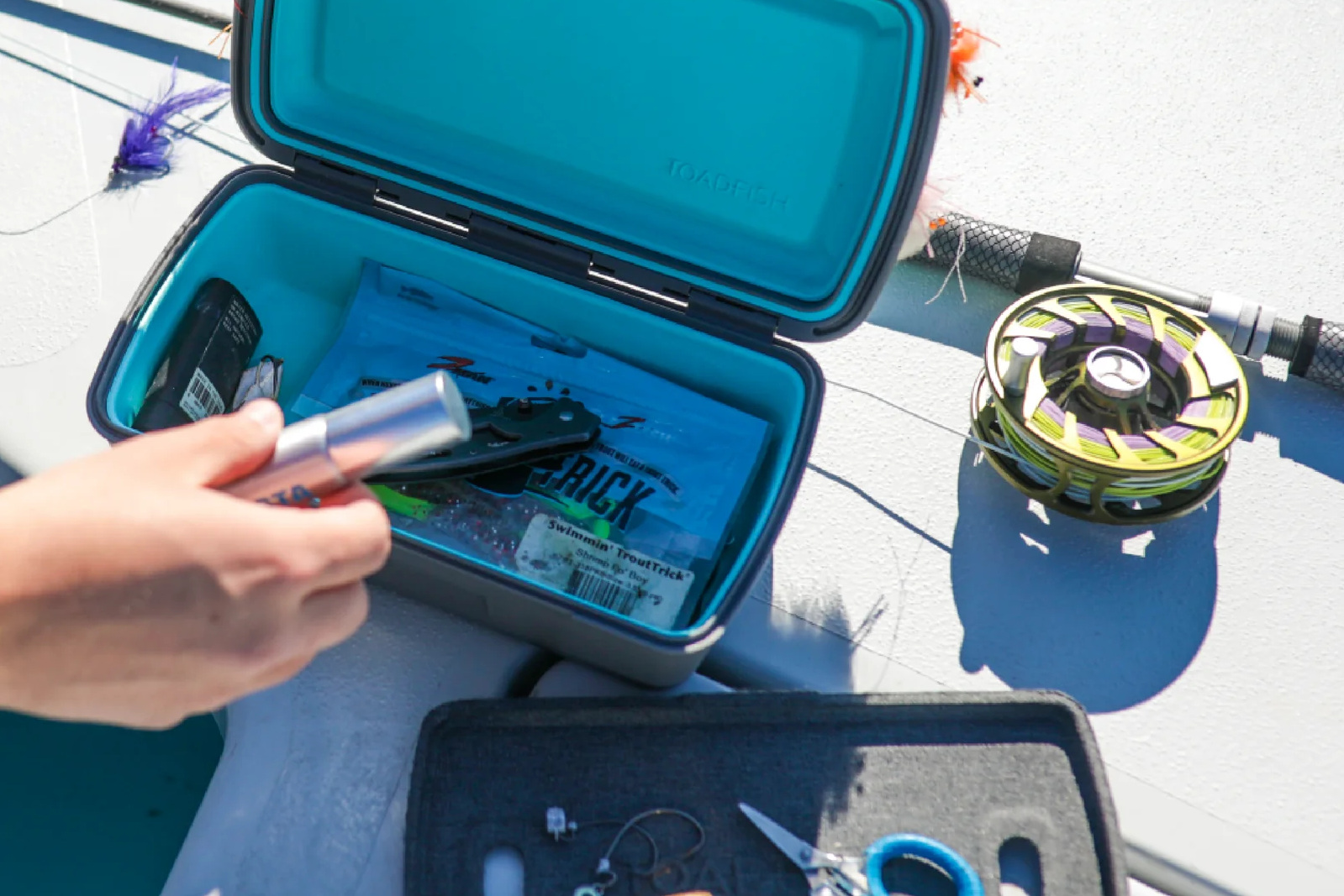 A Toadfish waterproof dry box opened to reveal various fishing lures and tackle items.