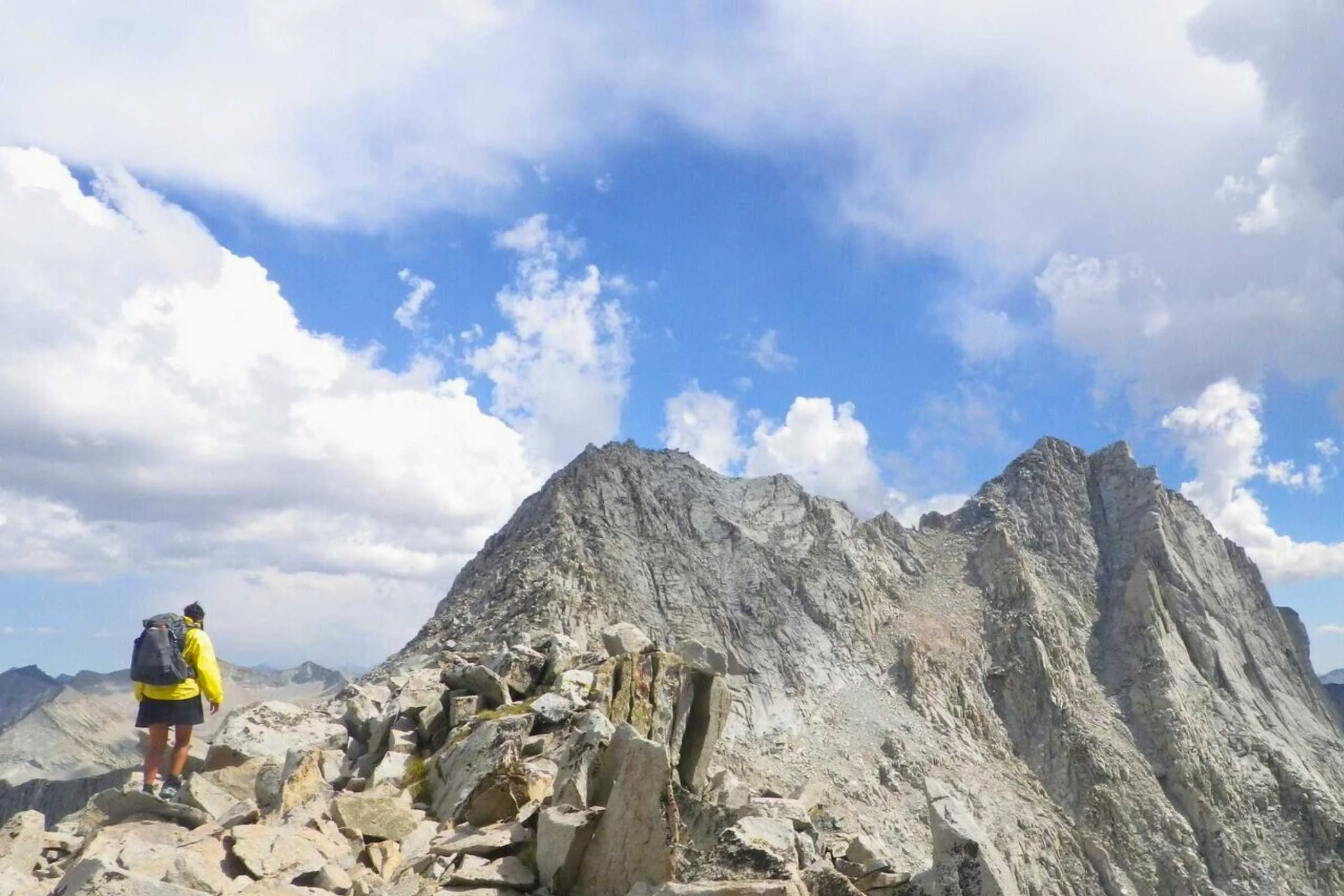 A hiker holding a Ricoh WG series camera while navigating a rocky mountain ridge.