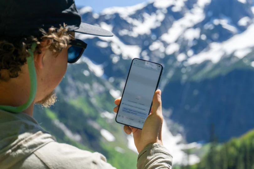 A person using a smartphone in a remote mountain area to access T-Mobile's Starlink satellite service.