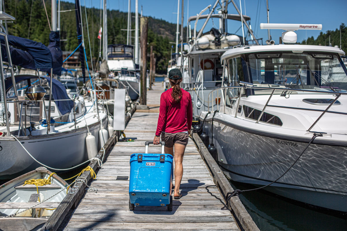 A white Yeti Roadie 48 wheeled cooler standing on a rocky shoreline.