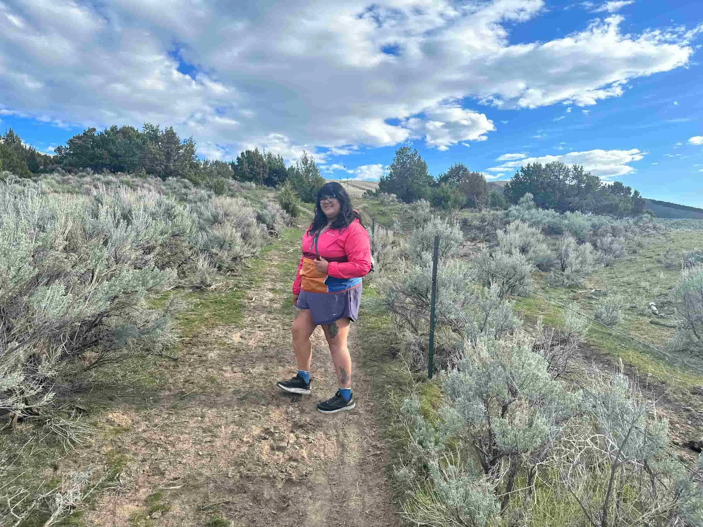 A hiker navigates through trail brush wearing a purple and orange Teca windbreaker.