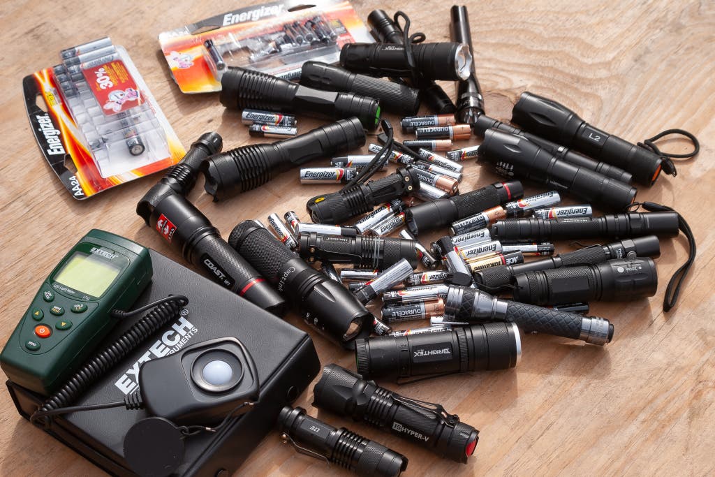 A large collection of flashlights and different battery sizes organized for comparison and testing.