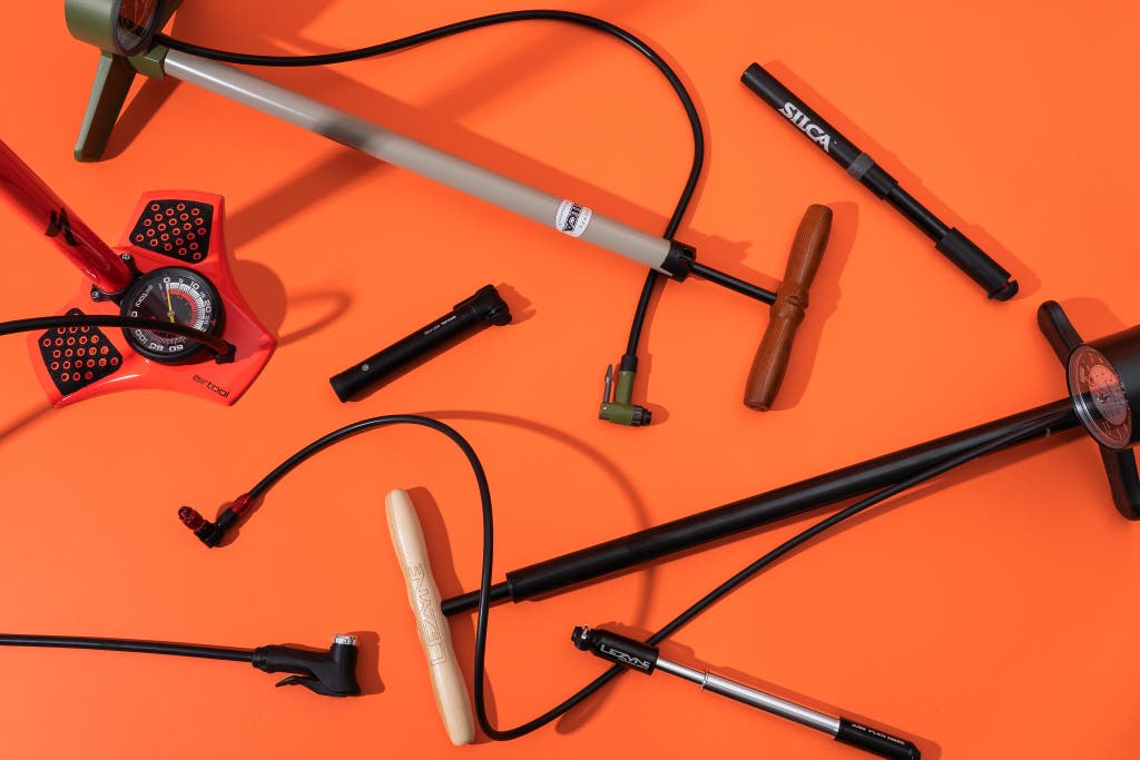 A wide variety of orange and black floor and mini bicycle pumps arranged on a bright orange background.